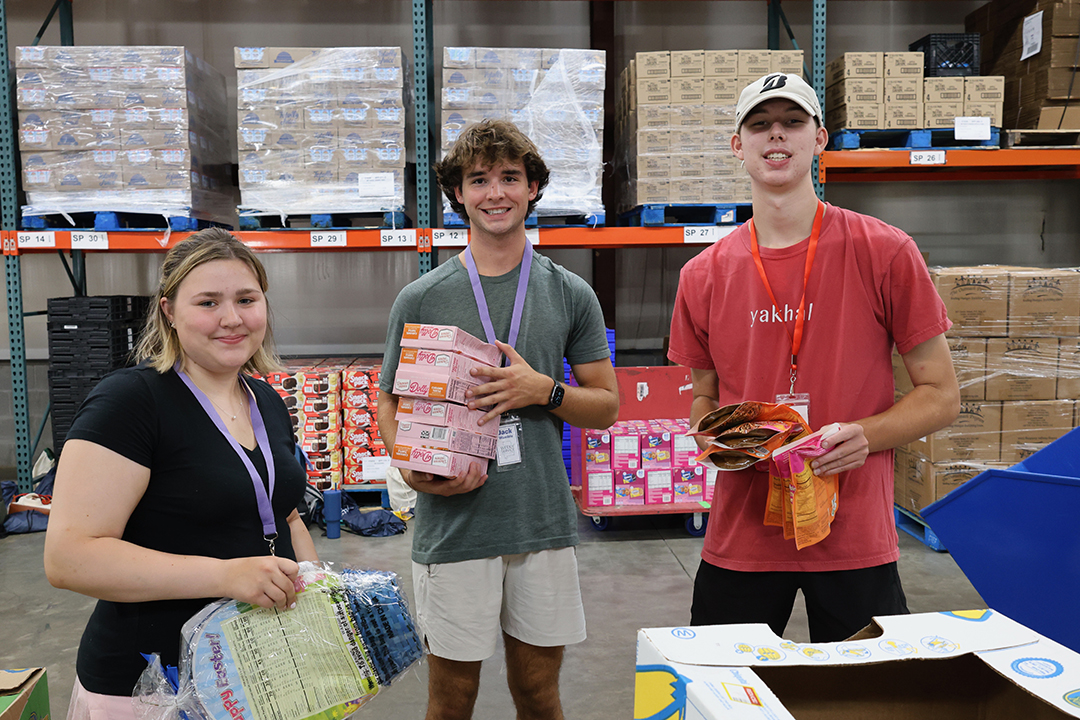 three students at the food bank holding items of food